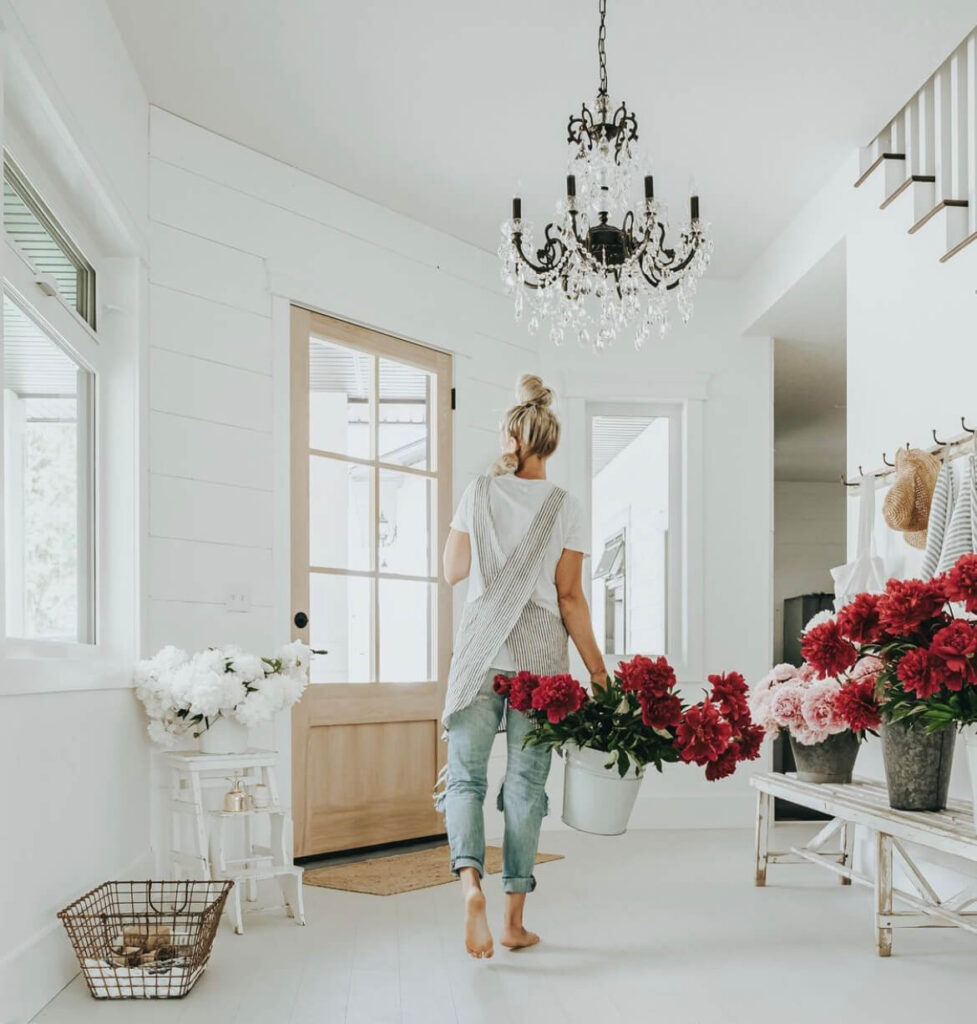 Brittany Dawn carrying peony flowers in a white Farmhouse with a crystal chandelier